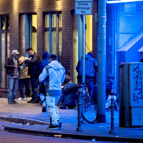 Menschen stehen abends vor einem Drogenkonsumraum im Frankfurter Bahnhofsviertel.  Einige davon sind blau beleuchtet.