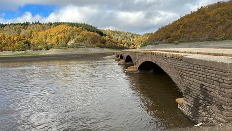 Eine alte Brücke mit vier gemauerten Bögen, unten durch fließt Wasser. Im Hintergrund ist ein Wald zu sehen.