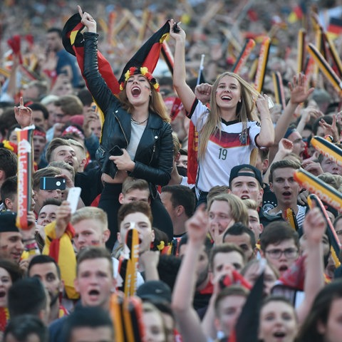 Tłum ludzi, wielu w niemieckich koszulkach piłkarskich, machających flagami.