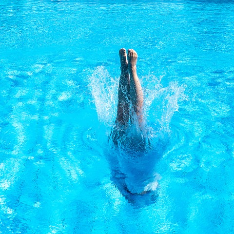 Eine Frau springt in einen leeren Swimmingpool. Nur ihre Füße sind zu sehen.