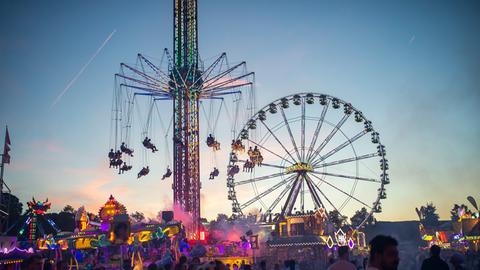 Menschenmenge auf einem großen Platz mit Riesenrad und Karussell vor abendlichem Himmel