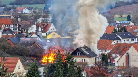 Brennende Scheune mit Rauchsäule inmitten vieler Fachwerkhäuser