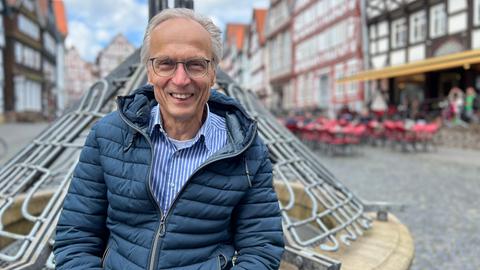 Michael Brückmann steht vor einem Brunnen auf dem Fritzlaer Marktplatz. Er hat graue Haare, trägt eine Brille und eine blaue Daunenjacke.