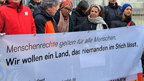 Mehrere Menschen stehen hinter einem Banner mit der Aufschrift:  "Menschenrechte gelten für alle Menschen. Wir wollen ein Land, das niemanden im Stich lässt."