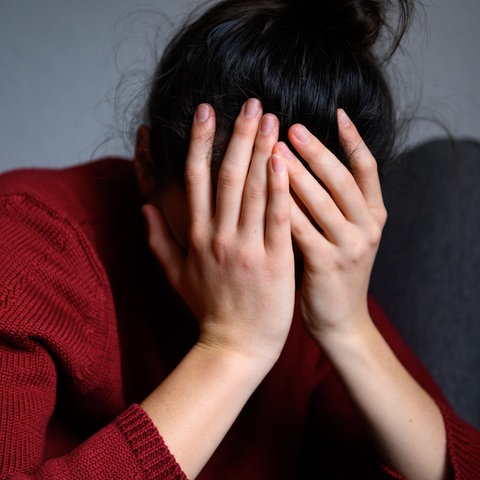 Eine Frau sitzt mit dem Kopf in den Händen auf einem Stuhl.