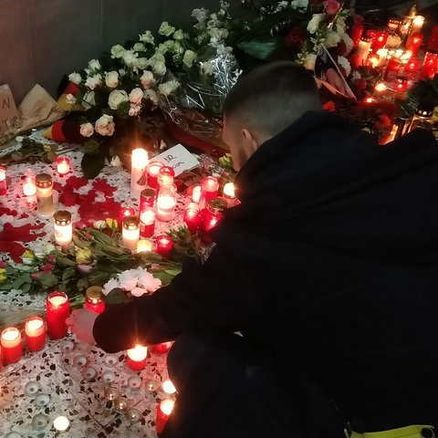 Ein improvisierte Gedenkstätte im Eingangsbereich eines Wohnhochhauses in Hanau-Kesselstadt. Ein Mann beugt sich über unzählige auf dem Boden abgelegte Blumen und Grablichter.