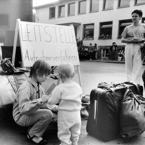 S/W-Foto: Frauen und Kinder mit viel Gepäck. In ihrer Mitte ein Schild mit der Aufschrift "Leitstelle Aufnahmeverfahren".