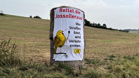 Banner auf einem großen Strohballen, der auf einem Acker steht, mit der Aufschrift: "Rettet die Jossolleraue - Wer Straßen baut, wird Verkehr ernten".