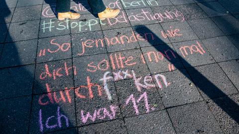 Bunte Kreideaufschrift auf einer Straße. Sie lautet: "Jemanden wie dich sollte man mal durchf**cken. Ich war 11." Dahinter angeschnitten die Füße einer Person, die daneben steht.