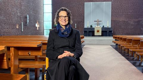 Eine Frau sitzt auf einem Stuhl in einer Kirche und lächelt in die Kamera