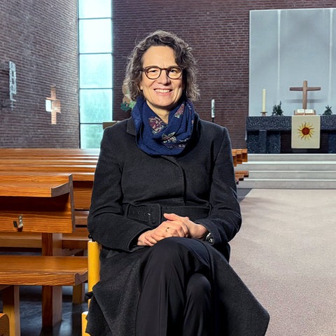 Eine Frau sitzt auf einem Stuhl in einer Kirche und lächelt in die Kamera