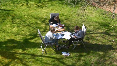 Schülerinnen erledigen in Kassel bei sonnigem Frühlingswetter im Garten ihre Aufgaben, die sie von der Schule für Zuhause gestellt bekommen haben. 