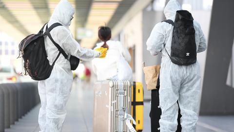 Chinesische Touristen in Schutzanzügen, mit Atemmasken und Handschuhen vor dem Terminal 1 des Frankfurter Flughafens mit ihren Koffern auf dem Weg zum Flugschalter. 