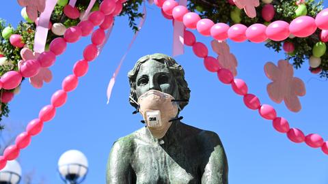 Die Brunnennymphe am bereits österlich geschmückten Brunnen in Bad Wildungen trägt eine Atemschutmaske. Viele Menschen scheinen die Appelle und Ausgangsbeschränkungen zu befolgen. 