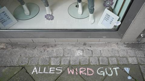 Alles wird gut !" ist mit farbiger Kreide vor einer geschlossenen Boutique auf den Asphalt geschrieben.