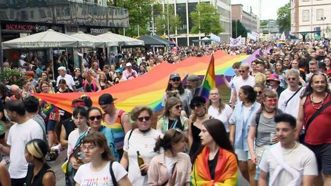 Teilnehmerinnen und Teilnehmer an der CSD-Parade in Darmstadt gehen durch eine Straße mit einer riesigen Regenbogenflagge