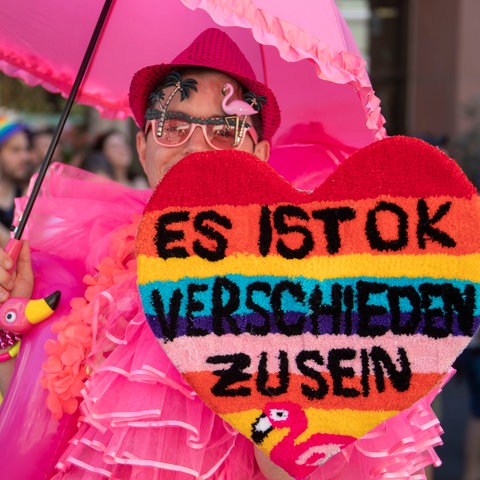 "Es ist ok, verschieden zu sein" steht auf dem selbst gebastelten Herzen eines in pink gekleideten Teilnehmers beim Christopher Street Day