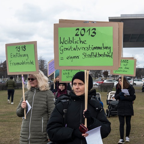 Mehrere Frauen bei einer Demonstration in Berlin, sie halten Plakate hoch mit den Botschaften "1918 Einführung Frauenwahlrecht" und "2013 Weibliche Genitalverstümmelung = eigener Straftatbestand"