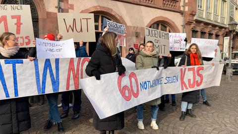 Menschen mit Plakaten haben sich vor dem Römer aufgestellt. Auf einem Plakat steht: "60 notwendige Stellen"