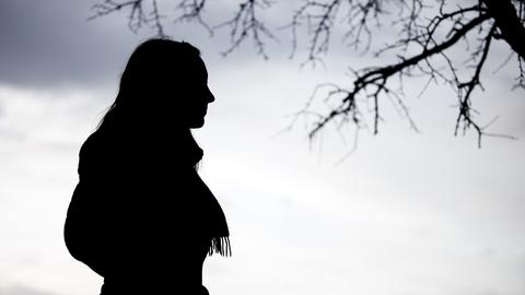 Eine Frau steht bei trübem Wetter unter einem kahlen Baum.