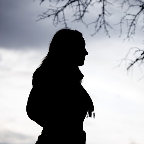 Eine Frau steht bei trübem Wetter unter einem kahlen Baum.