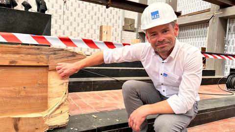 Ein Mann mit Helm kniet in der Elisabethkirche und kratzt auf einem der Holzleimträger herum