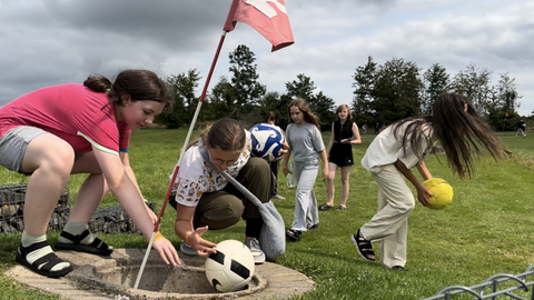 Ukrainische Kinder holen beim Fußball-Golf in Breitscheid einen Ball aus dem Loch.