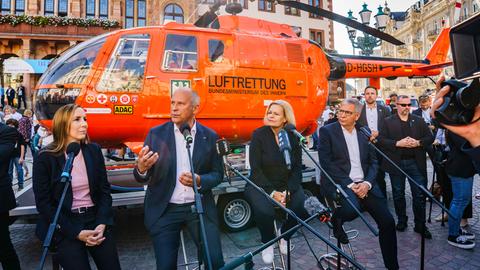 Astrid Wallmann (l-r, CDU), Präsidentin des Landtags, Innenminister Roman Poseck (CDU), Bundesinnenministerin Nancy Faeser (SPD) und Wiesbadens OB Gert-Uwe Mende (SPD) sitzen vor einem Rettungshubschrauber.