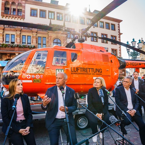 Astrid Wallmann (l-r, CDU), Präsidentin des Landtags, Innenminister Roman Poseck (CDU), Bundesinnenministerin Nancy Faeser (SPD) und Wiesbadens OB Gert-Uwe Mende (SPD) sitzen vor einem Rettungshubschrauber.