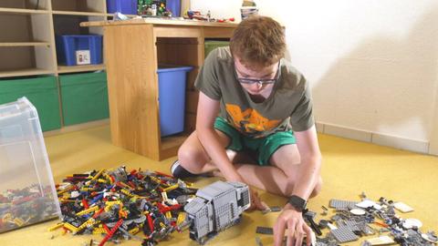 Ein Jugendlicher mit Brille sitzt auf dem Boden seines Kinderzimmers und spielt mit Legosteinen