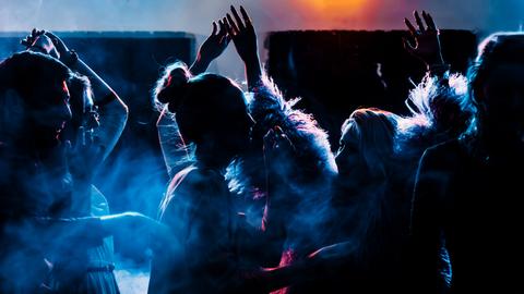 Foto von feiernden, tanzenden jungen Menschen mit viel Schatten und bläulichem Licht.