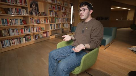 Noam sitzt auf einem Sessel in der Bibliothek des Jüdischen Museums in Frankfurt. Auf seinen dunkelbraunen, kurzen Haaren trägt er die traditionelle orthodoxe Kopfbedeckung Kippa. 