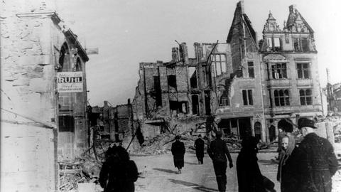 Menschen gehen über den zerstörten Gießener Marktplatz 1944 