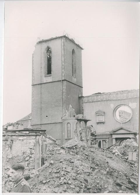 Schwarz-Weiß-Foto einer Kirche, von der der quadratische Turm zu sehen ist und Schäden am Dach zu erkennen sind