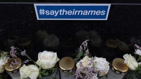 Grablichter und Blumen stehen unter einem blauen Schild mit der Aufschrift "#saytheirnames"