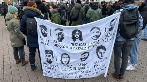 Demonstrierende mit Banner, auf denen Gesichter und Namen der Anschlagsopfer zu erkennen sind