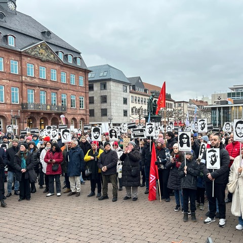 Demonstrierende mit Banner, auf denen Gesichter und Namen der Anschlagsopfer zu erkennen sind