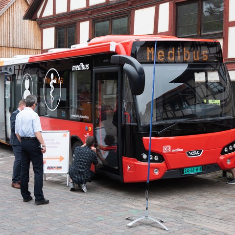 Ein sogenannter Medibus, eine Arztpraxis auf Rädern, steht in einem hessischen Dorf. Menschen begutachten das Fahrzeug.