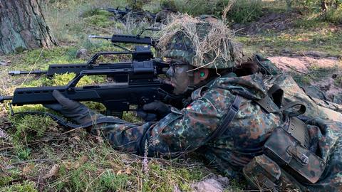 Rekrutin in Tarn-Uniform liegt auf Waldboden und zielt mit Gewehr