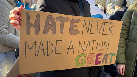 Demonstratin hält braunen Plakat mit Aufschift: "Hate never made a nation great"