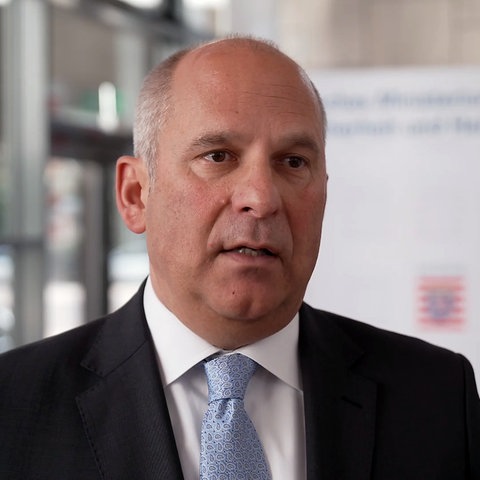 Porträt von Hessens Innenminister Roman Poseck in schwarzem Anzug und hellblauer Krawatte, mit ganz kurzgeschnittenen grauen Haaren, braunen Augen und einem vollen Gesicht