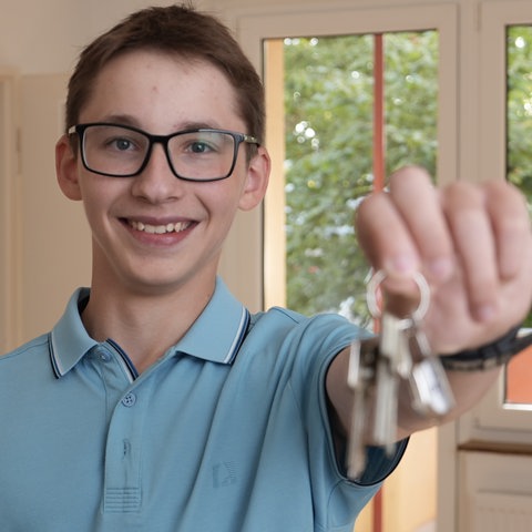 Ein Jugendlicher (16 Jahre) mit Brille und einem hellblauen Poloshirt hält einen Schlüsselbund in die Kamera