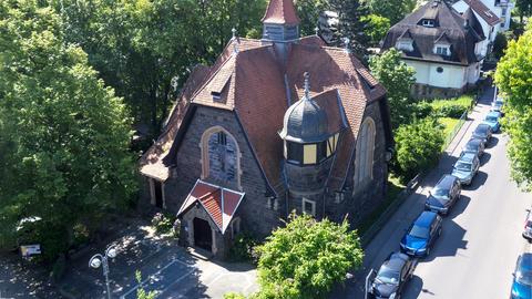 Ein Gebäude mit braunem Dach, dunkelbraunen Backsteinwänden und hohen Fenstern steht inmitten von Bäumen.