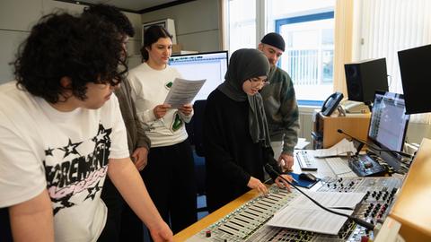 Fünf junge Frauen und Männer stehen in einem Aufnahmestudio an einem Mischpult.