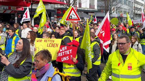 Ein Demonstrationszug: Teilnehmer halten Poster mit Aufschriften wie "Wir retten Leben" und "Wer rettet uns?" und "Verdi".