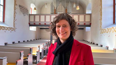 Eine Frau steht mit einer roten Jacke und lockigen Haaren in einer Kirche