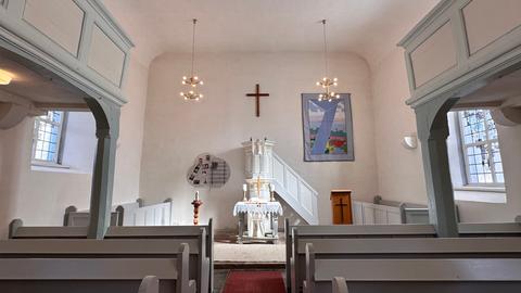 Ein leerer Kirchenraum in weiß gehalten mit Altar und Holzempore