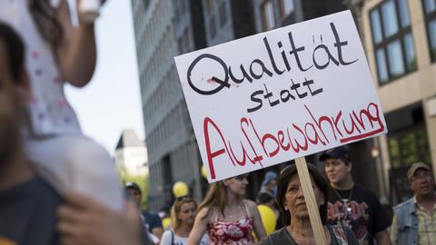 Erwachsene und Kinder in einer Straße beim Demonstrieren für bessere Kinderbetreuung. Jemand hält ein Schild hoch mit der Aufschrift "Qualität statt Aufbewahrung".