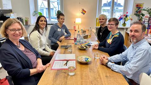 Berivan Sekerci sitzt gemeinsam mit der Staatssekretärin und Mitgliedern des Queeren Zentrums dort an einem großen Holztisch zum Kennenlerngespräch, die Teilnehmer lächeln in die Kamera.