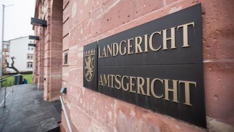 Im Bildvordergrund Schild mit der Aufschrift "Landgericht Amtsgericht" an einer Sandsteinmauer. Im Hintergund unscharf die Fassade und der EIngang des dazugehörigen Gebäudes.